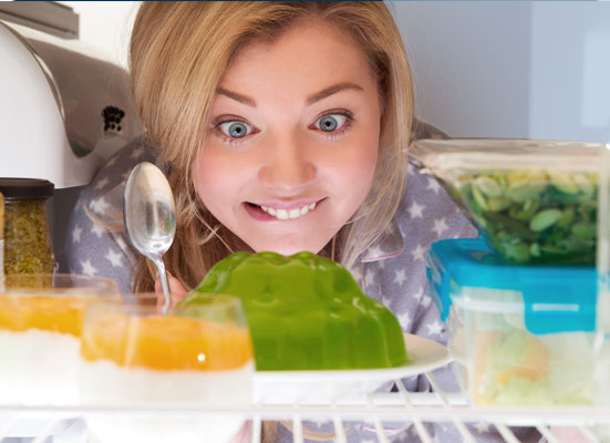 Woman peering into refrigerator with spoon in hand looking at a gelatin mold