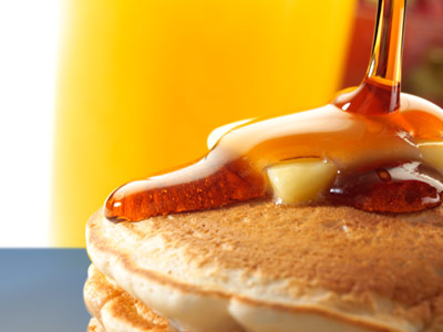 Syrup being poured on top of a stack of pancakes