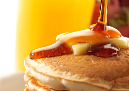 Syrup being poured over a stack of pancakes